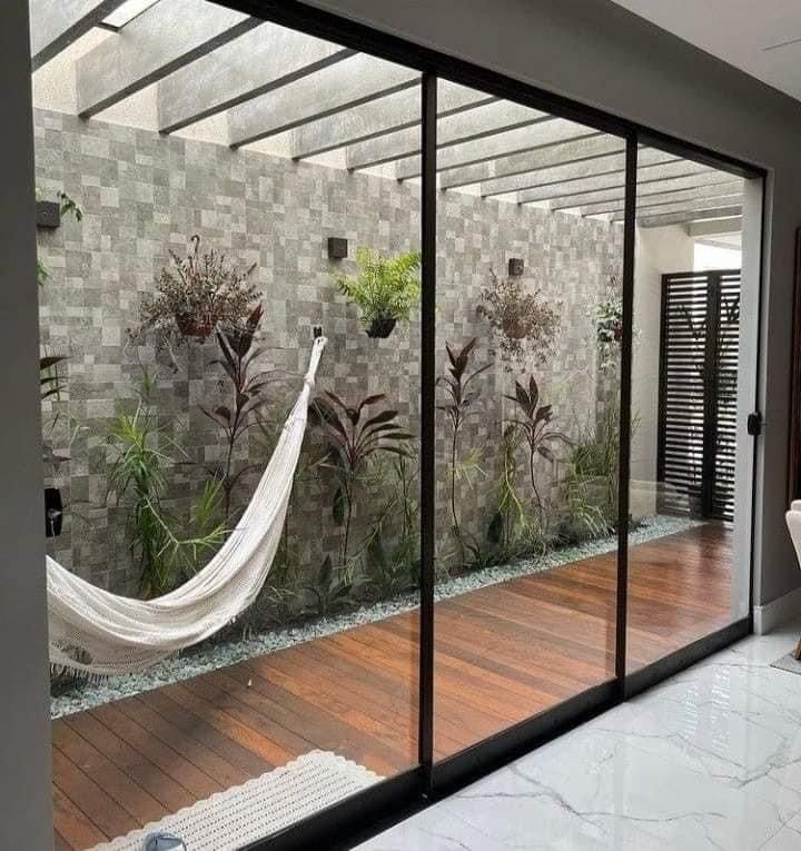 Mampara corrediza de cuatro hojas que abre a un patio interior con muro de piedra y hamaca