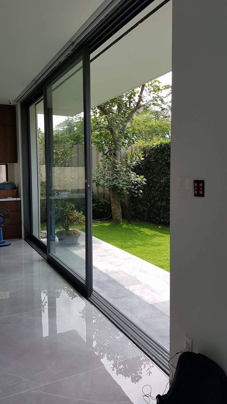 Mampara corrediza de gran formato con riel inferior, abierta hacia el jardín de una vivienda